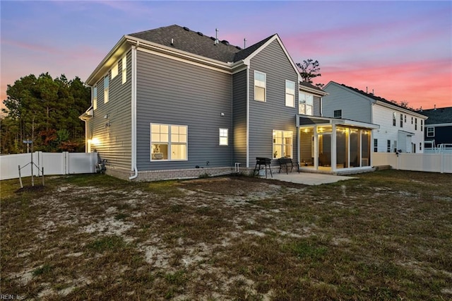 back house at dusk featuring a yard, a sunroom, and a patio