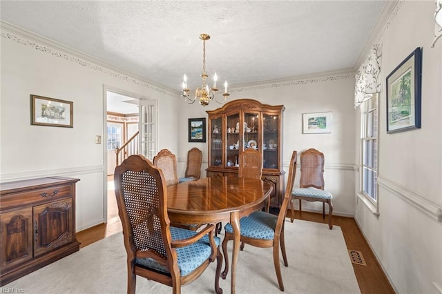 dining space featuring ornamental molding, a textured ceiling, a chandelier, and light hardwood / wood-style flooring