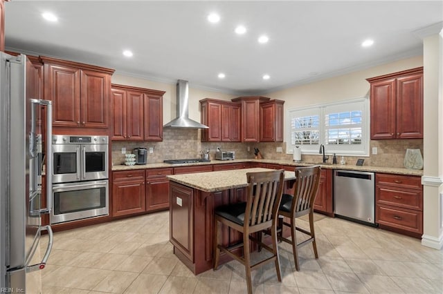 kitchen featuring appliances with stainless steel finishes, a breakfast bar, a center island, light stone countertops, and wall chimney range hood