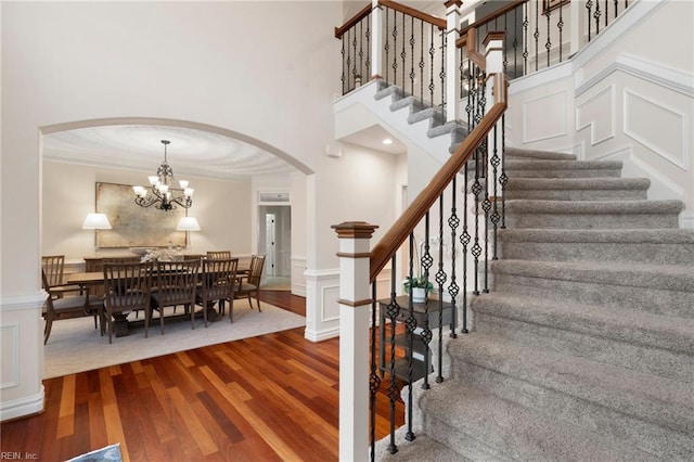 stairway with hardwood / wood-style floors, ornamental molding, a chandelier, and a high ceiling