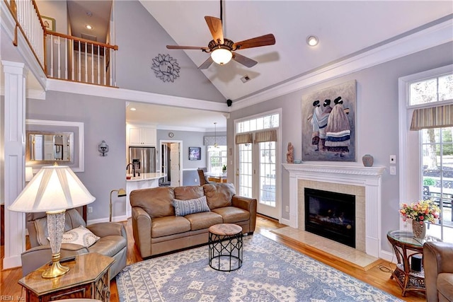 living room with ceiling fan, high vaulted ceiling, ornamental molding, light hardwood / wood-style floors, and a tiled fireplace