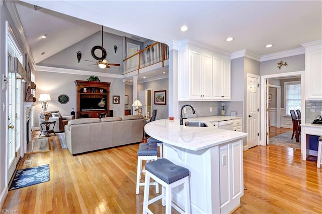 kitchen featuring sink, a kitchen breakfast bar, dishwasher, light stone countertops, and white cabinets