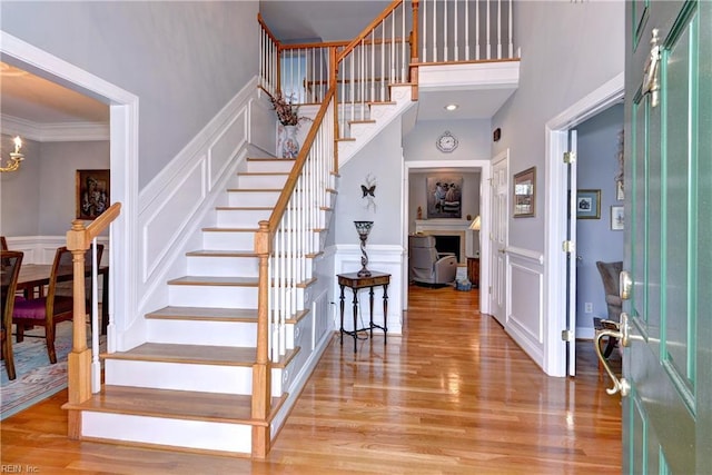 foyer entrance with crown molding, a towering ceiling, an inviting chandelier, and light wood-type flooring