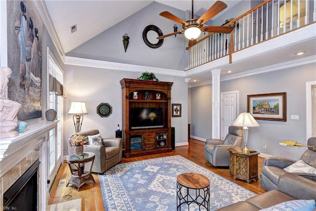 living room featuring high vaulted ceiling, decorative columns, a tile fireplace, and light wood-type flooring