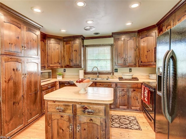 kitchen with sink, butcher block counters, a center island, light hardwood / wood-style floors, and black appliances