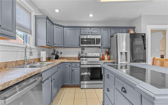 kitchen with gray cabinetry, sink, light tile patterned floors, and stainless steel appliances