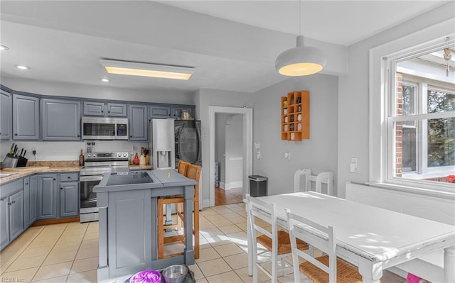 kitchen featuring light tile patterned floors, appliances with stainless steel finishes, gray cabinetry, hanging light fixtures, and light stone counters