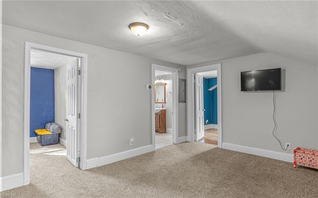 unfurnished bedroom featuring ensuite bathroom, electric panel, vaulted ceiling, and carpet