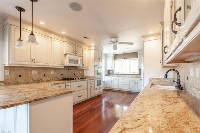 kitchen with decorative light fixtures, white cabinetry, sink, light stone countertops, and white appliances