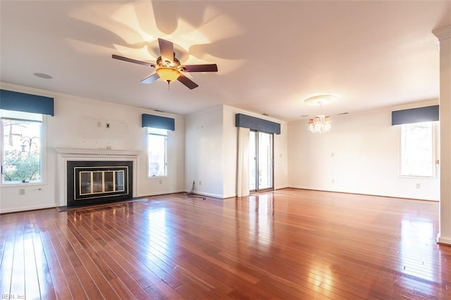 unfurnished living room featuring hardwood / wood-style flooring, crown molding, a healthy amount of sunlight, and ceiling fan with notable chandelier