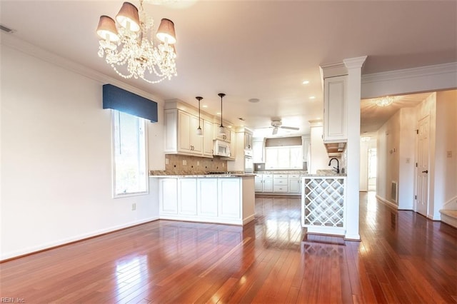 kitchen with white cabinetry, decorative light fixtures, kitchen peninsula, and backsplash