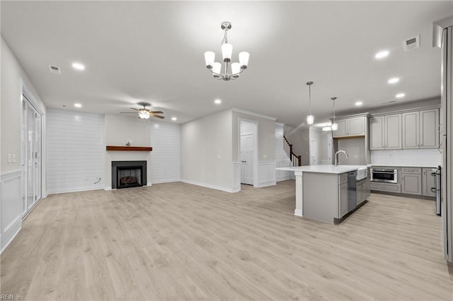 kitchen featuring gray cabinets, decorative light fixtures, a kitchen island with sink, stainless steel dishwasher, and light hardwood / wood-style floors