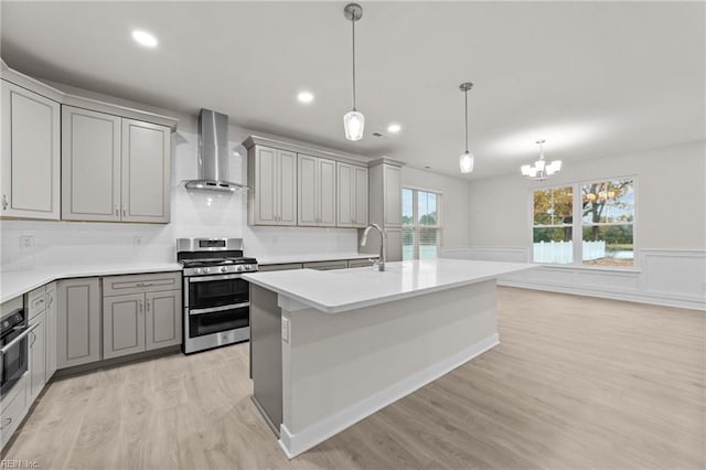 kitchen featuring gray cabinetry, double oven range, a kitchen island with sink, light hardwood / wood-style floors, and wall chimney exhaust hood