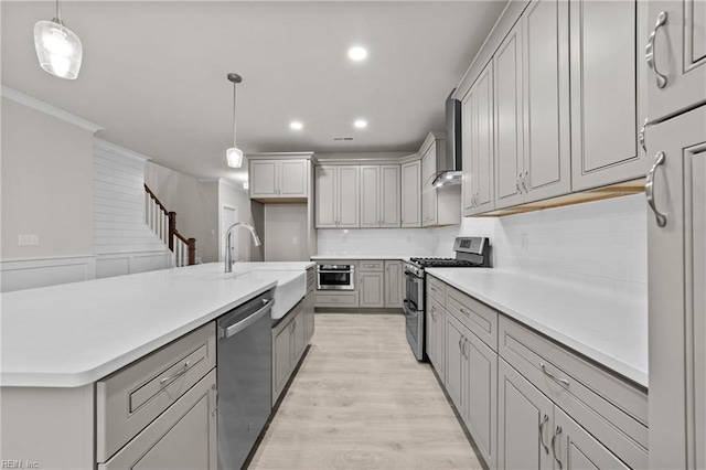 kitchen with gray cabinetry, hanging light fixtures, stainless steel appliances, light hardwood / wood-style floors, and a center island with sink