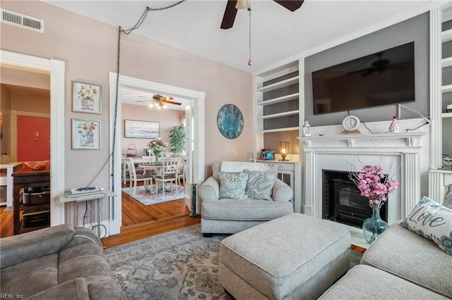 living room with hardwood / wood-style floors, a fireplace, ceiling fan, and built in shelves