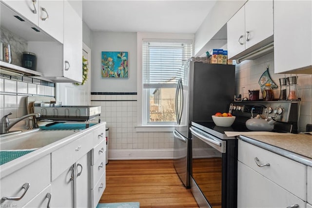 kitchen with sink, white cabinetry, tile walls, light wood-type flooring, and appliances with stainless steel finishes