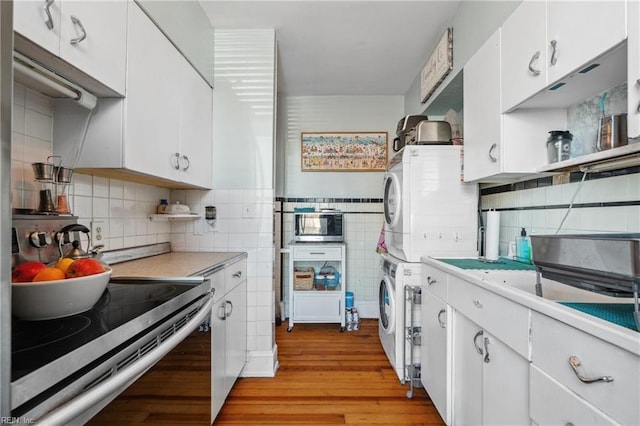 kitchen with stacked washer and clothes dryer, tile walls, light hardwood / wood-style flooring, stainless steel appliances, and white cabinets