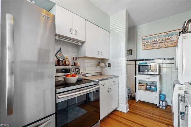 kitchen featuring stainless steel appliances, white cabinetry, tile walls, and light hardwood / wood-style floors