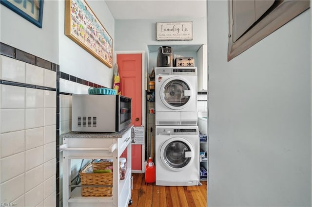 clothes washing area featuring hardwood / wood-style flooring, stacked washer and dryer, and tile walls