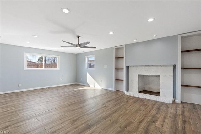 unfurnished living room with hardwood / wood-style floors, built in shelves, a brick fireplace, and ceiling fan