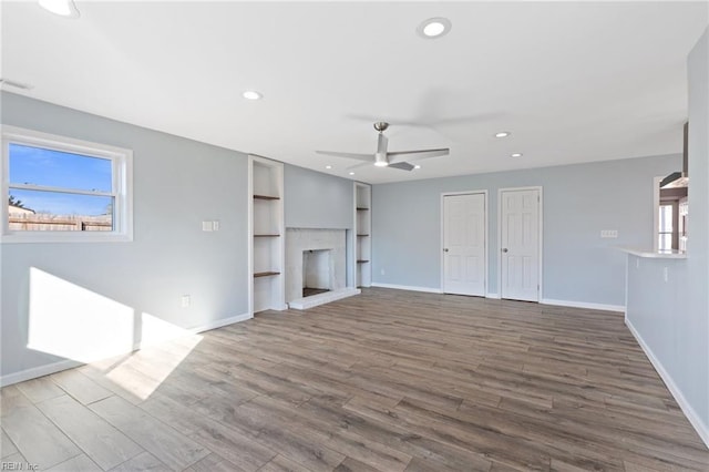 unfurnished living room with a brick fireplace, wood-type flooring, ceiling fan, and plenty of natural light