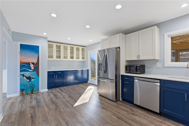 kitchen with appliances with stainless steel finishes, blue cabinets, white cabinetry, sink, and light wood-type flooring