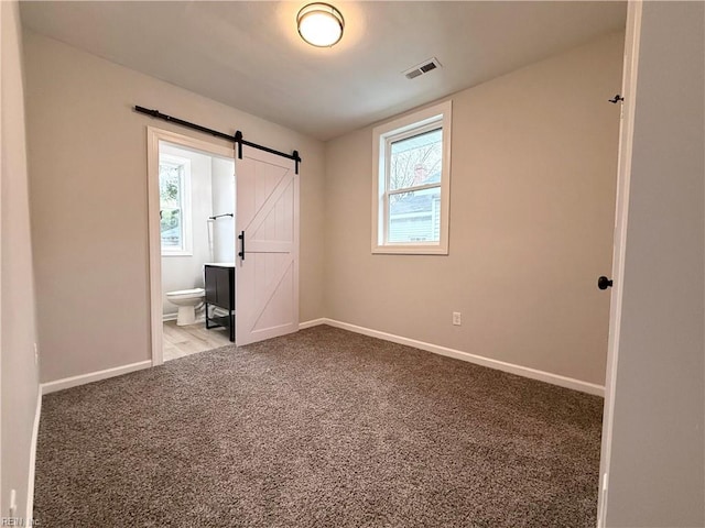 unfurnished bedroom with ensuite bathroom, a barn door, and carpet floors