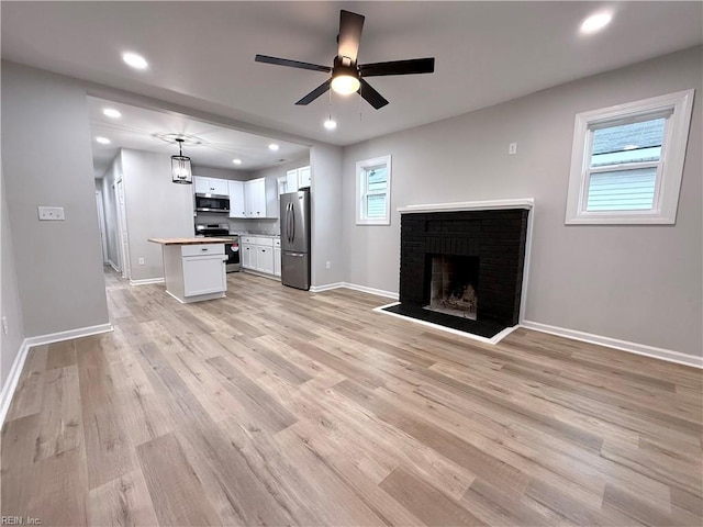 unfurnished living room featuring a fireplace, light hardwood / wood-style flooring, ceiling fan, and plenty of natural light