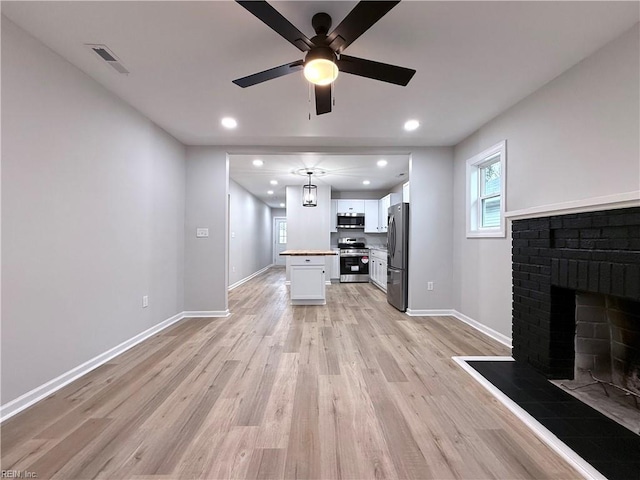 unfurnished living room with ceiling fan, a fireplace, and light hardwood / wood-style floors