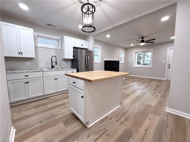 kitchen featuring decorative light fixtures, sink, white cabinets, wooden counters, and stainless steel fridge