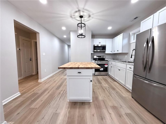 kitchen featuring sink, white cabinetry, wooden counters, decorative light fixtures, and stainless steel appliances