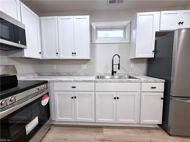 kitchen featuring stainless steel appliances, sink, light hardwood / wood-style flooring, and white cabinets