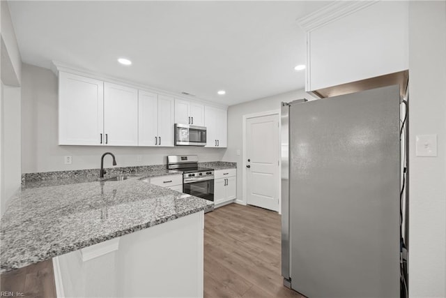 kitchen featuring appliances with stainless steel finishes, sink, white cabinets, kitchen peninsula, and light stone countertops