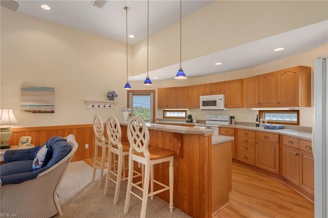 kitchen featuring decorative light fixtures, a center island, wooden walls, white appliances, and light hardwood / wood-style floors