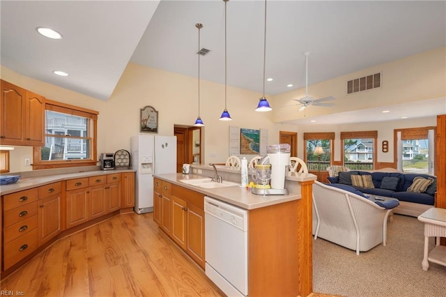 kitchen with sink, light wood-type flooring, pendant lighting, white appliances, and a kitchen island with sink