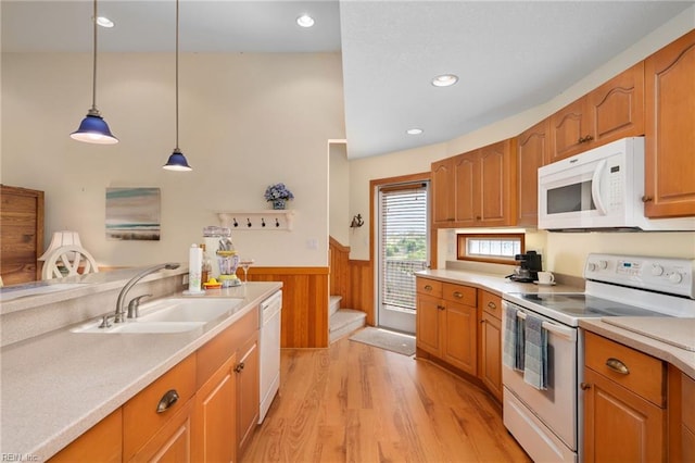 kitchen with wooden walls, sink, hanging light fixtures, white appliances, and light hardwood / wood-style flooring