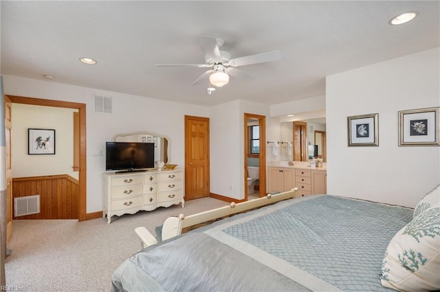 bedroom with ceiling fan, light colored carpet, connected bathroom, and wood walls