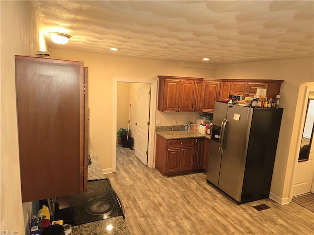 kitchen featuring cooktop, stainless steel refrigerator with ice dispenser, light stone counters, and light hardwood / wood-style floors