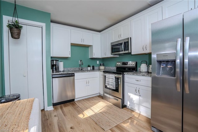 kitchen featuring white cabinetry, light stone countertops, stainless steel appliances, and light wood-type flooring