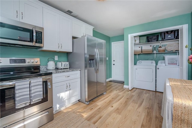 kitchen with washing machine and clothes dryer, light hardwood / wood-style flooring, appliances with stainless steel finishes, light stone countertops, and white cabinets