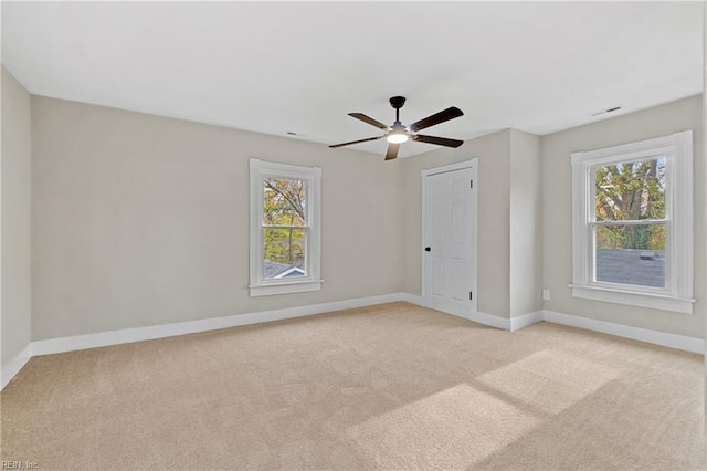 spare room with a wealth of natural light, light colored carpet, and ceiling fan