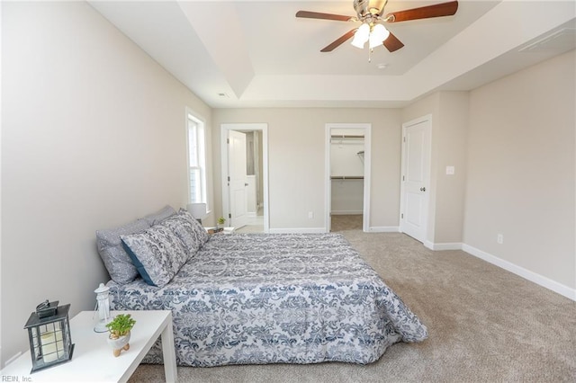 carpeted bedroom with a tray ceiling, a closet, ceiling fan, and a spacious closet