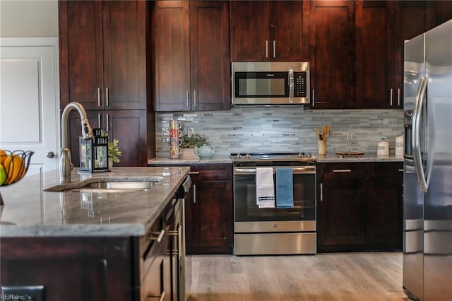 kitchen featuring sink, stainless steel appliances, tasteful backsplash, light hardwood / wood-style floors, and light stone countertops