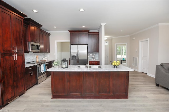 kitchen with light stone counters, an island with sink, appliances with stainless steel finishes, and sink