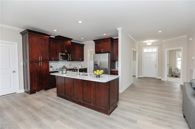 kitchen with sink, appliances with stainless steel finishes, tasteful backsplash, light hardwood / wood-style floors, and an island with sink