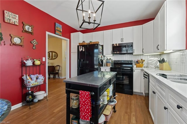 kitchen featuring hanging light fixtures, light hardwood / wood-style flooring, white cabinets, and black appliances