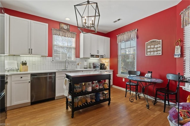 kitchen featuring sink, white cabinetry, light hardwood / wood-style floors, decorative light fixtures, and stainless steel dishwasher