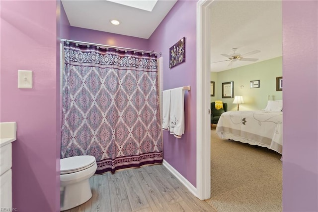 bathroom with ceiling fan, a skylight, vanity, wood-type flooring, and toilet