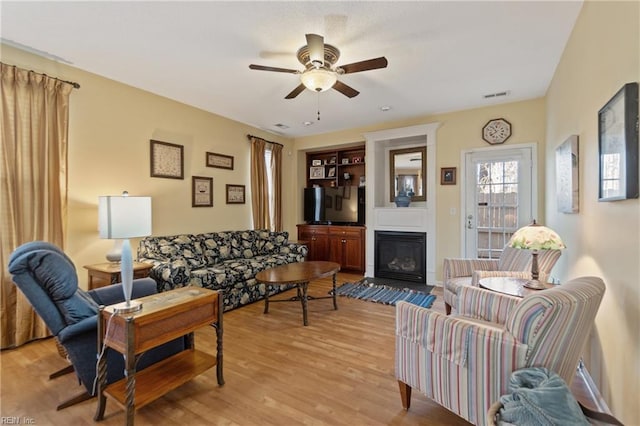 living room with ceiling fan, a large fireplace, and light hardwood / wood-style floors