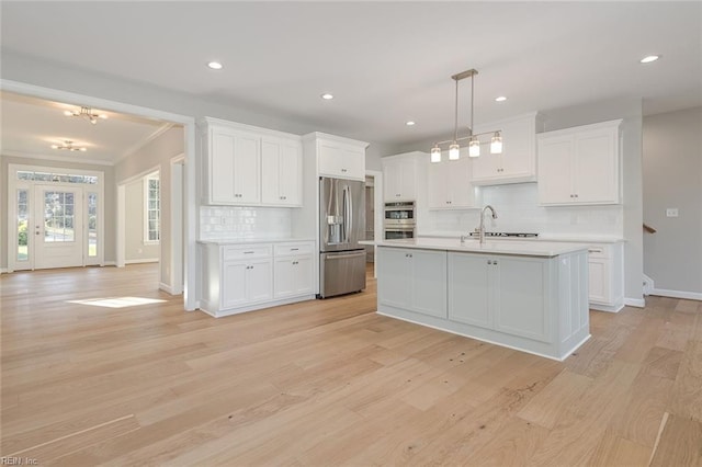 kitchen with light hardwood / wood-style flooring, appliances with stainless steel finishes, white cabinetry, a kitchen island with sink, and decorative light fixtures